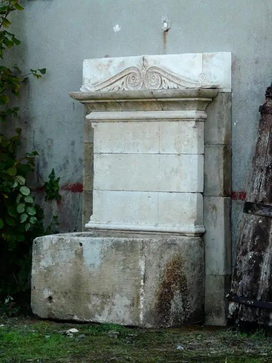 Fontaine murale composée d'un bac monolithe ancien et d'un fronton en pierre à corniche Directoire
