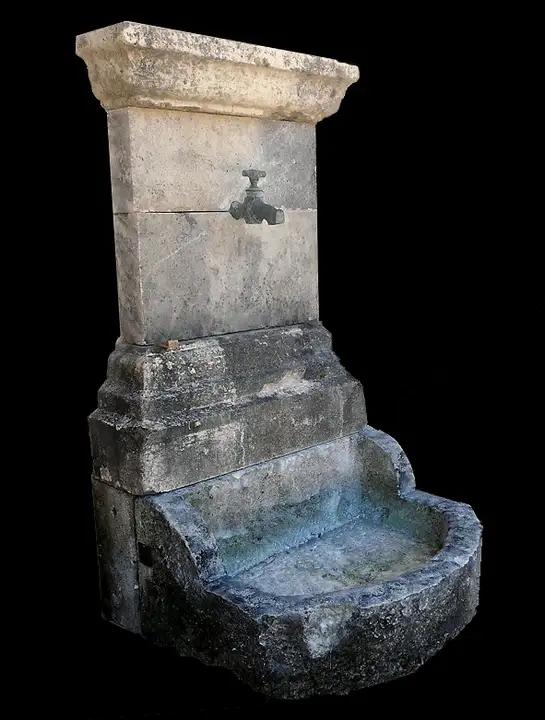 Fontaine d'applique en pierre de Charente composée d'un bac demi-lune,  d'un fronton et d'un robinet en bronze