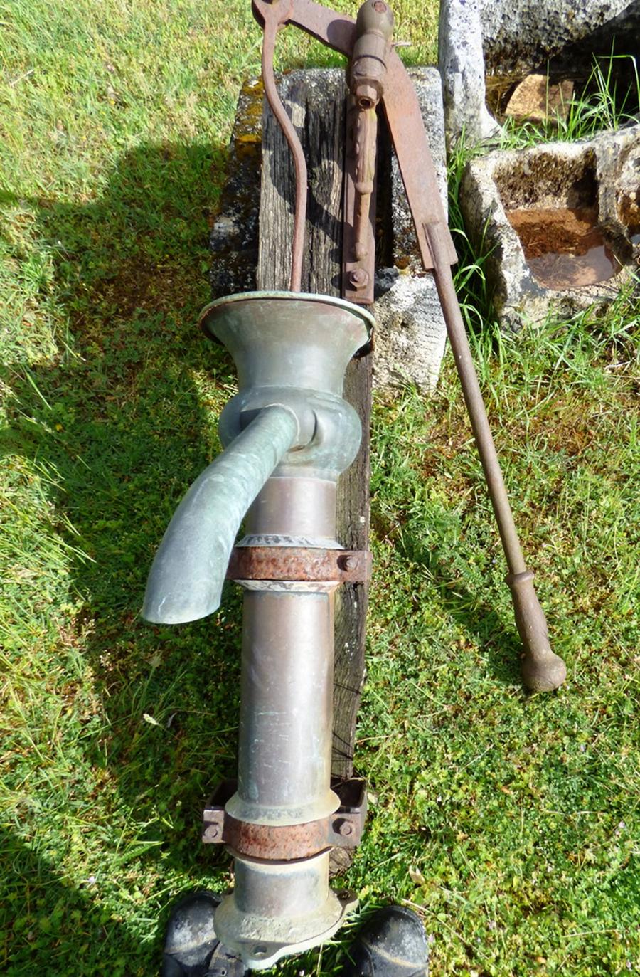 Pompe ancienne à bras en cuivre pour puits ou cuisine fixée sur un support en bois